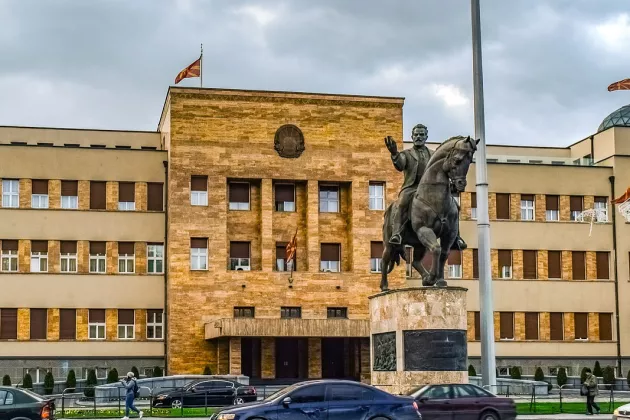 A statue of a person on a horse. The statue sits in front of a beige building.